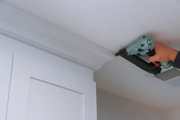 Carpenter nailing crown moldings in the kitchen cabinets framing trim worker using air brad nail gun