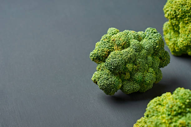 istock Scattered fresh bunches of broccoli on scratched dark concrete desk. Space for text 1185232955