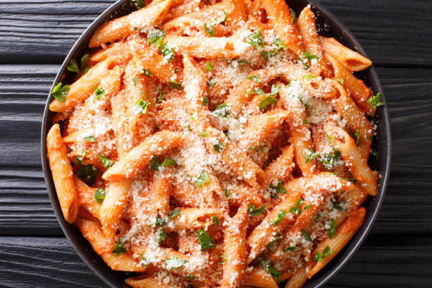 penne alla vodka is tender pasta tossed in a rich and delicious tomato, vodka and cream sauce, all topped with parmesan cheese close-up. Horizontal top view penne alla vodka is tender pasta tossed in a rich and delicious tomato, vodka and cream sauce, all topped with parmesan cheese close-up in a plate on the table. Horizontal top view from above vodka sauce stock pictures, royalty-free photos & images