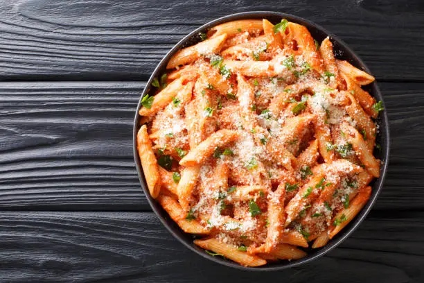 Penne alla Vodka is a classic Italian pasta dish made with penne in a creamy tomato and vodka sauce close-up in a plate on the table. Horizontal top view from above