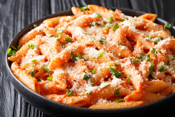 penne alla vodka is tender pasta tossed in a rich and delicious tomato, vodka and cream sauce, all topped with parmesan cheese close-up. horizontal penne alla vodka is tender pasta tossed in a rich and delicious tomato, vodka and cream sauce, all topped with parmesan cheese close-up in a plate on the table. horizontal vodka photos stock pictures, royalty-free photos & images