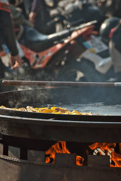 Fried potatoes in a large frying pan. Grilled vegetables on motorcycle festival background. Blurred motorcycles in the background. Parking for bikers. Motorcycle food interchange.