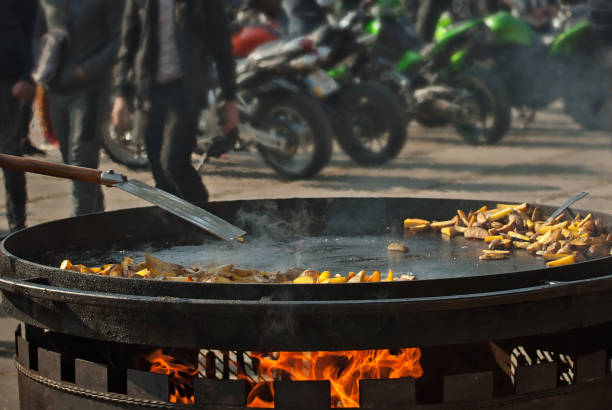 Fried potatoes in a large frying pan. Grilled vegetables on motorcycle festival background. Blurred motorcycles in the background. Parking for bikers. Motorcycle food interchange.