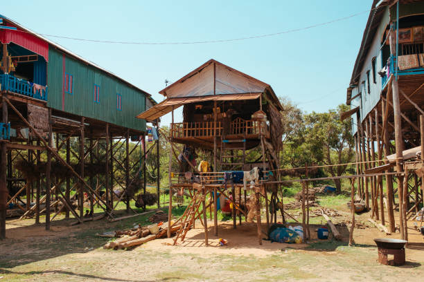 casas residenciais flutuantes da vila em pólos de madeira e na estrada vermelha do solo em kampong phluk cambodia perto do lago tonle sap - pier rowboat fishing wood - fotografias e filmes do acervo