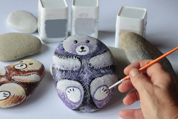 istock hand with small brush painting a bear shape on a stone 1185243784