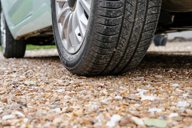 Ground level view of a new car, showing the rear tyre and tread together with the alloy wheel Parked on a gravel driveway and showing some of its light blue paint. driveway stock pictures, royalty-free photos & images