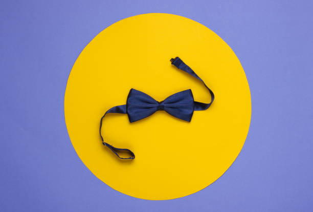 Bow tie on purple paper background with yellow circle in the middle. Top view.