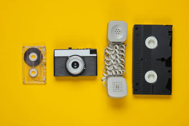 istock Outdated handset, audio and video cassette, retro camera on a yellow background. Top view 1185251029
