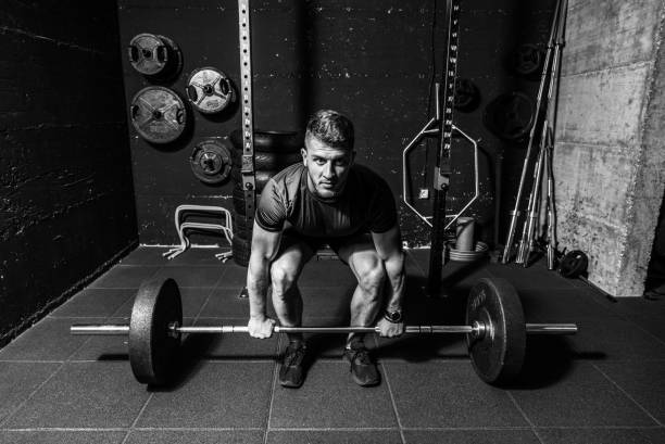 istock Young strong fit muscular sweaty man with big muscles doing heavy barbell weight lifting workout cross training in the gym real people black and white 1185251237