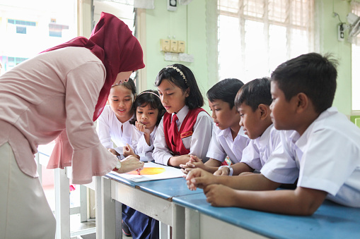 A female Malay teacher and her students participating in a group discussion inside a classroom.