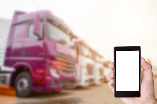 Hand with a phone on the background of parking with trucks. The concept of the application for truckers on the phone to search for goods, control the time of work and rest and find a parking spot, copy space, navigation