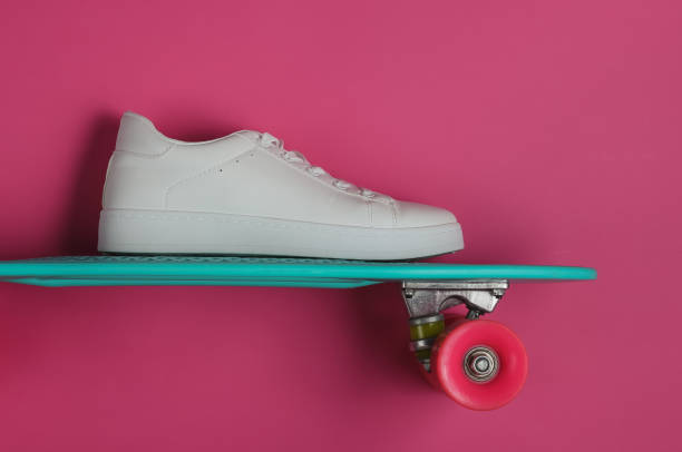 istock Stylish white sneakers with cruiser board on pink background. Summertime fun. Studio shot, top view. 1185255145