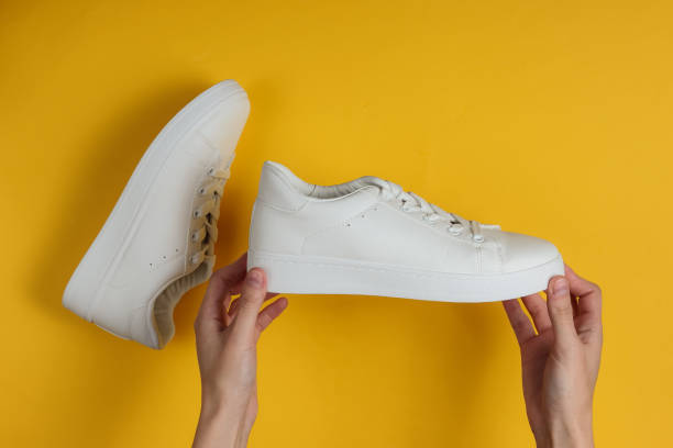 istock Female hands hold white stylish sneakers on a yellow studio background. Top view. 1185255195