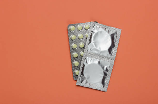 kondome in verpackung, antibabypillen auf rosa hintergrund. ansicht von oben. das konzept der sexuellen bewahrung - contraceptive pill birth control pill sex education stock-fotos und bilder