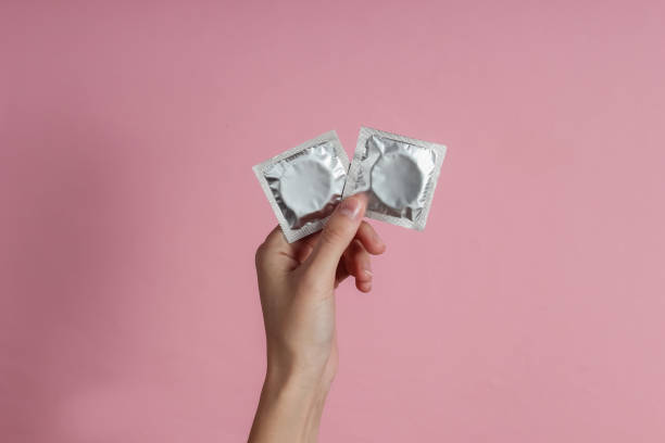 분홍색 배경에 콘돔을 들고 있는 여성 손. 맨 위 보기. 성적 보존의 개념 - condom sex education contraceptive aids 뉴스 사진 이미지