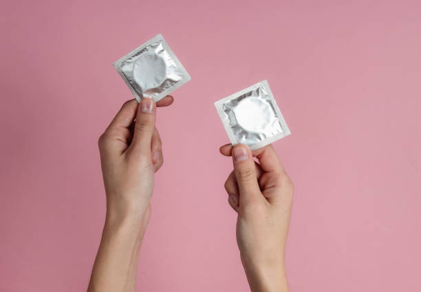 mains femelles retenant le condom sur le fond rose. vue du haut. le concept de préservation sexuelle - condom sex education contraceptive aids photos et images de collection