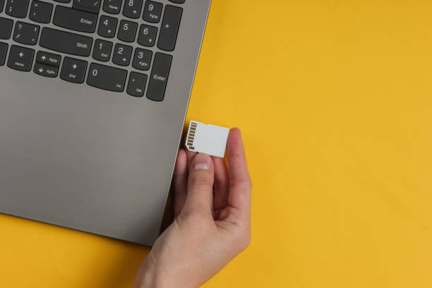 istock Female hand inserts SD memory card into laptop on a yellow background. Top view 1185255299