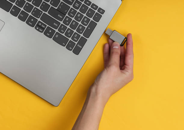 weibliche hand verbindet usb-flash-laufwerk mit laptop auf gelbem papierhintergrund. ansicht von oben - usb stock-fotos und bilder