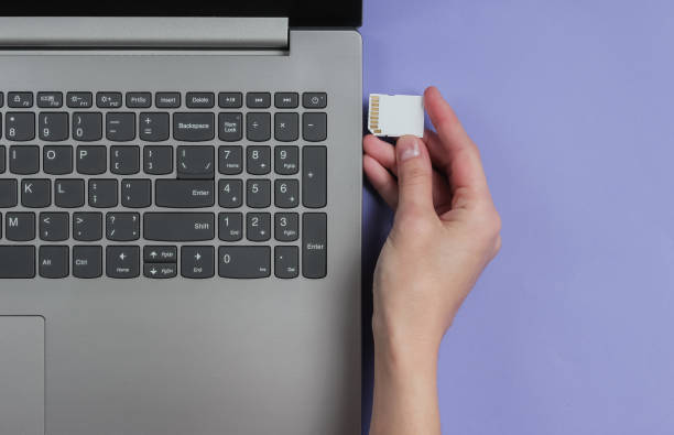 istock Female hand inserts SD memory card into laptop on purple background. Top view 1185255319