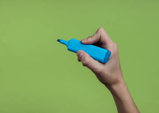 istock Female hand holds a blue felt-tip pen on a green background. Top view 1185255329