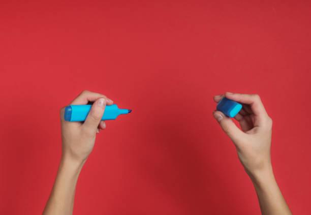 Female hand holds a blue felt-tip pen on red background. Top view