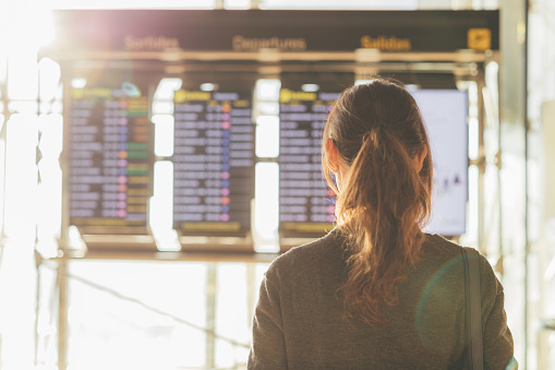 Rear view of young woman looking at flight information board in airport