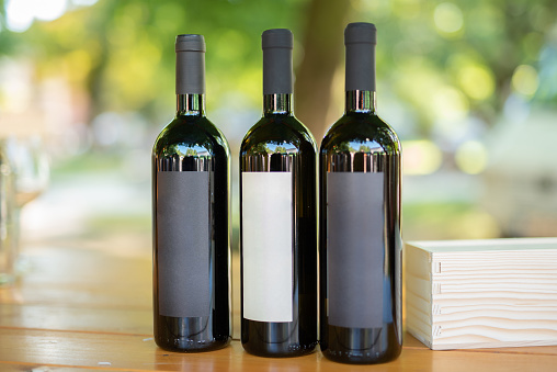 Three bottles of red wine with blank labels on wooden table outdoors