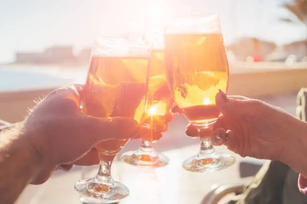 Photo of Group of happy friends drinking beer outdoors together - hands with beer glasses clinking on a sunny backgraund - concept of friendship and celebration