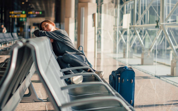 Young tired woman sleeping alone in empty airport with her hand luggage, waiting flight - transportation, low cost traveling, delayed or cancelled flight concept stock photo
