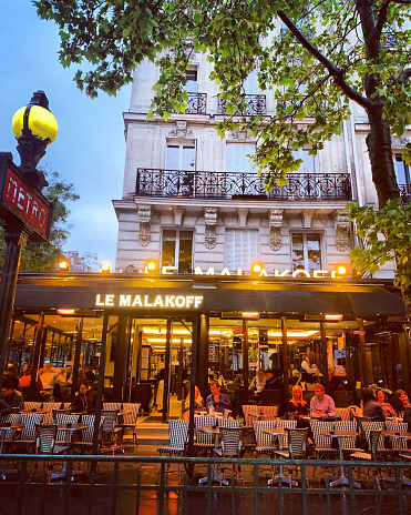 Paris, France - May 10, 2019: Le Malakoff cafe with people dining inside and outside on a rainy night
