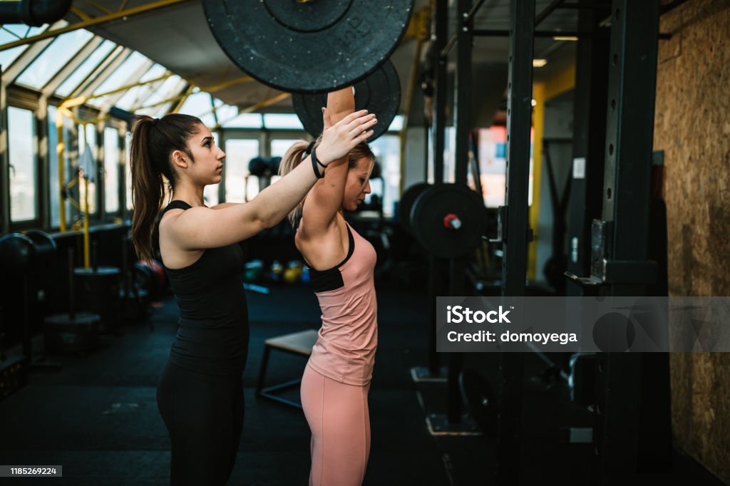 Woman lifting weights with a help of fitness instructor Young woman exercising in the gym and lifting weights with a help of female fitness instructor Fitness Instructor Stock Photo