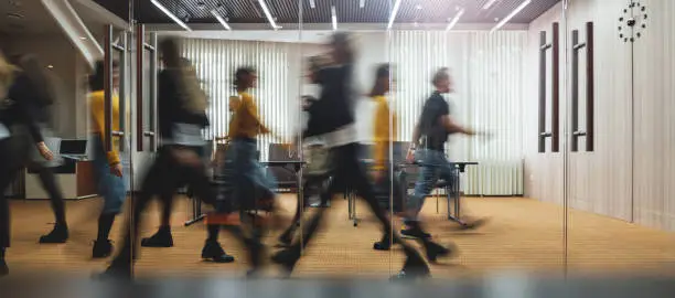 Photo of Businesspeople walking at modern office. Group of business employees at coworking center. Motion blur. Concept work process. Wide image