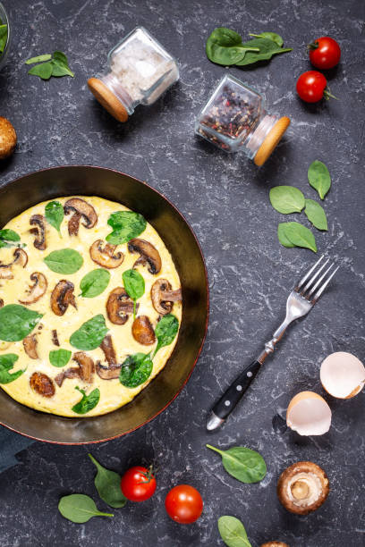 istock Omelette with mushrooms and spinach in iron pan on black stone background. 1185282051