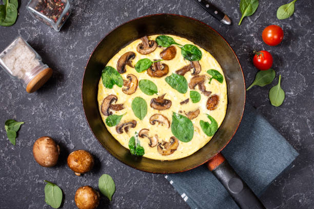 istock Omelette with mushrooms and spinach in iron pan on black stone background. 1185282145