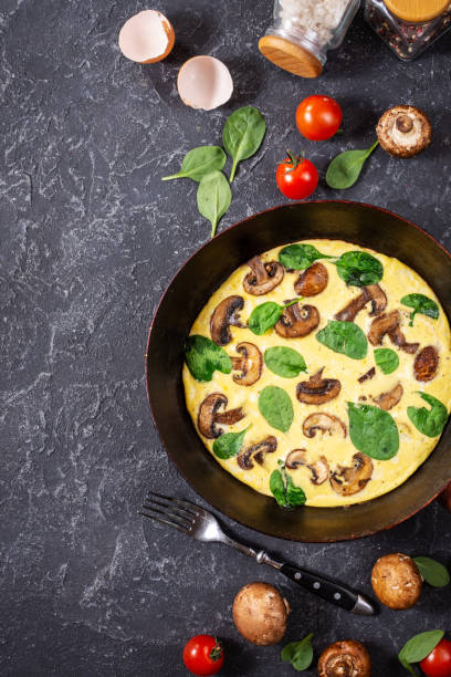 istock Omelette with mushrooms and spinach in iron pan on black stone background. 1185282197