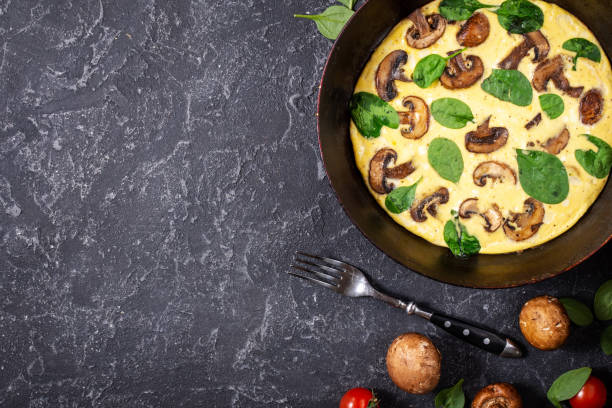 istock Omelette with mushrooms and spinach in iron pan on black stone background. Top view 1185282527