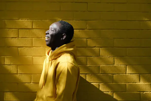 Portrait Of African Young Man Looking Away And Smiling. Copy Space On Yellow Wall In Background.