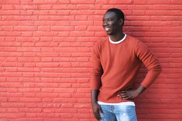 Portrait Of African Young Man Looking Away And Smiling. Copy Space On Red Wall In Background.