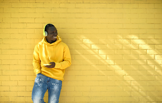 African Young Man Listening Music Leaning On Yellow Wall