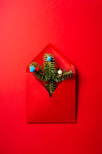 istock Christmas composition. Red envelope with fir branches and pastel colored wool balls on red  background. 1185284487