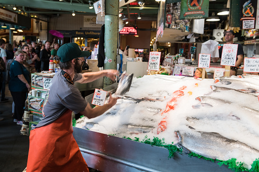Seattle, USA - Jul 3, 2019: A fish Monger at Pike Place Market throwing a fish for tourists late in the day.