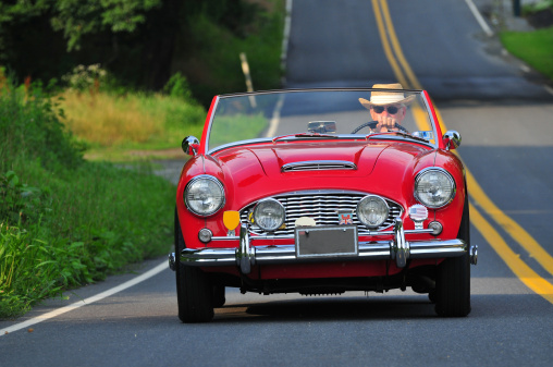 senior man driving a classic red sports car on a country road