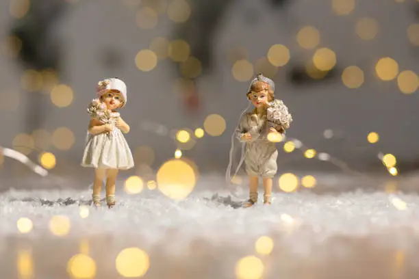 Photo of Decorative Christmas-themed figurines. Statuette boy and girl with a bouquet of flowers. Christmas tree decoration. Festive decor, warm bokeh lights.
