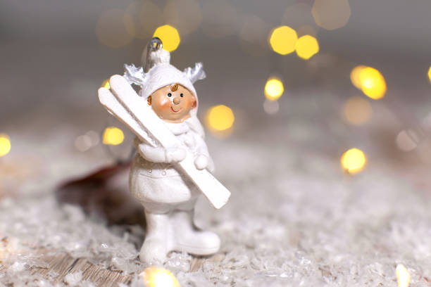 Decorative Christmas-themed figurines. Statuette A little man in a white suit with white skis. Christmas tree decoration. Festive decor, warm bokeh lights.