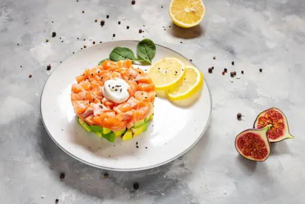 Delicious avocado and salted salmon tartar on concrete background