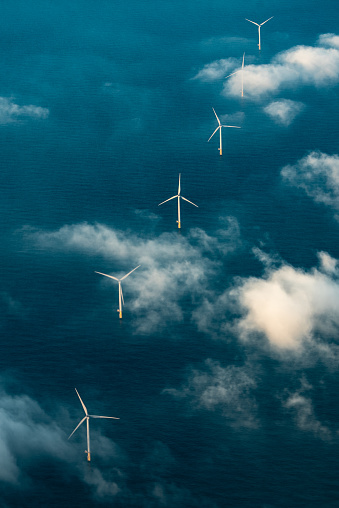 Row of wind turbines at sea seen with clouds from above