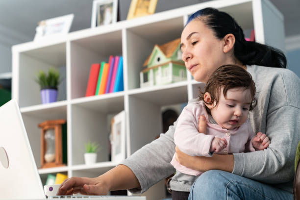 istock Mother Working From Home While Holding Her Baby In Living Room 1185307184
