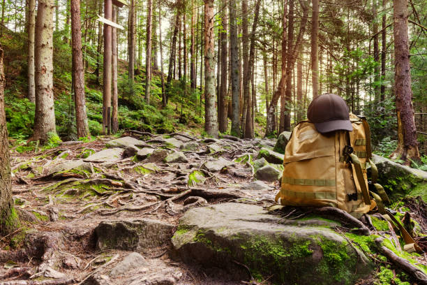 Forest hill sunny day landscape photo with rocks, moss, roots and tactical backpack standing with black cap, horizontally oriented.