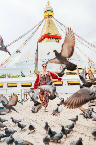 istock Beautiful female sincerely smiling and going by square through pigeons flock with Boudhanath Stupa - the largest spherical stupas in Nepal. Traveling around the world concept image. 1185310786