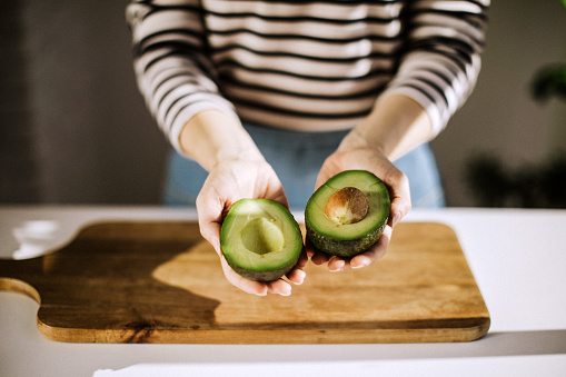 Unrecognizable woman holding in her hands opened avocado, close up